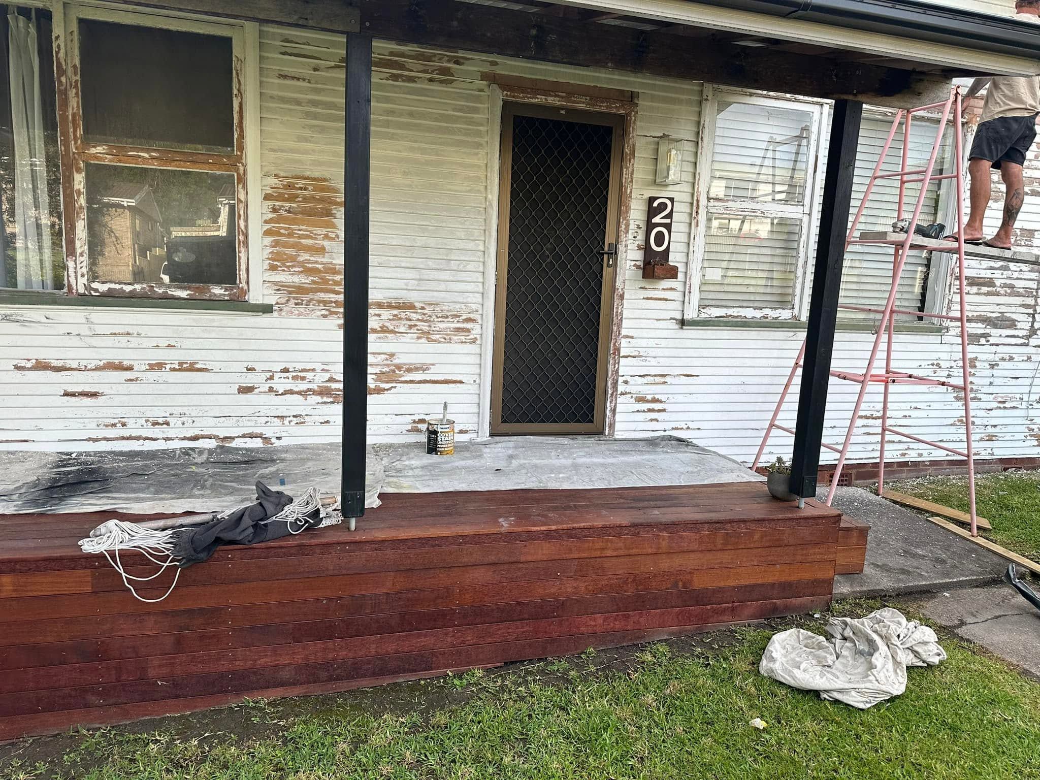 Weatherboard house front with peeling paint and ladders before repainting