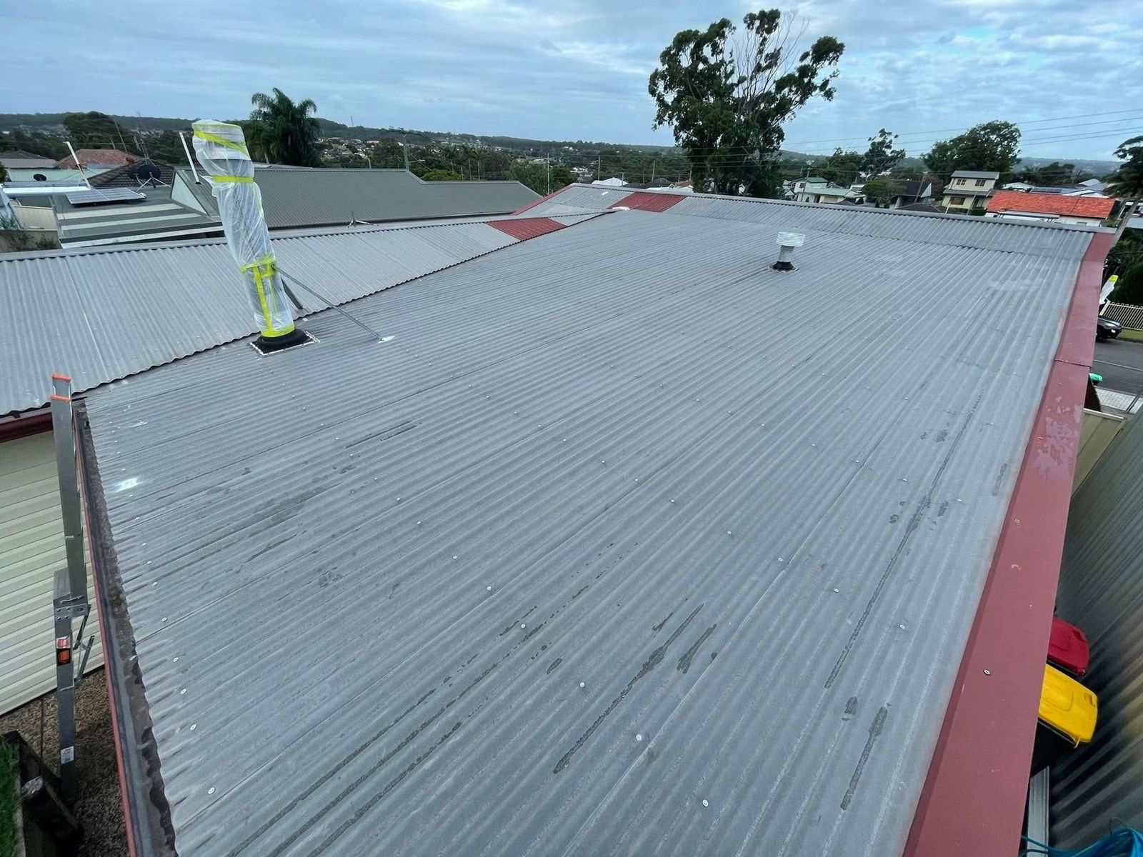 Roof mid-restoration in Newcastle, faded grey sheets beside freshly painted red sections